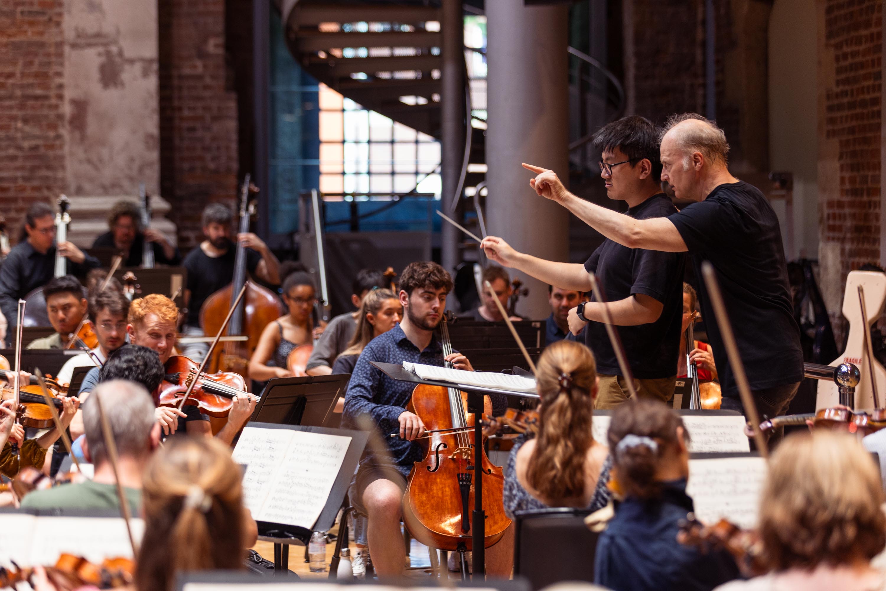 Gianandrea Noseda guiding an OA conductor, in front of an orchestra of LSO and OA musicians.