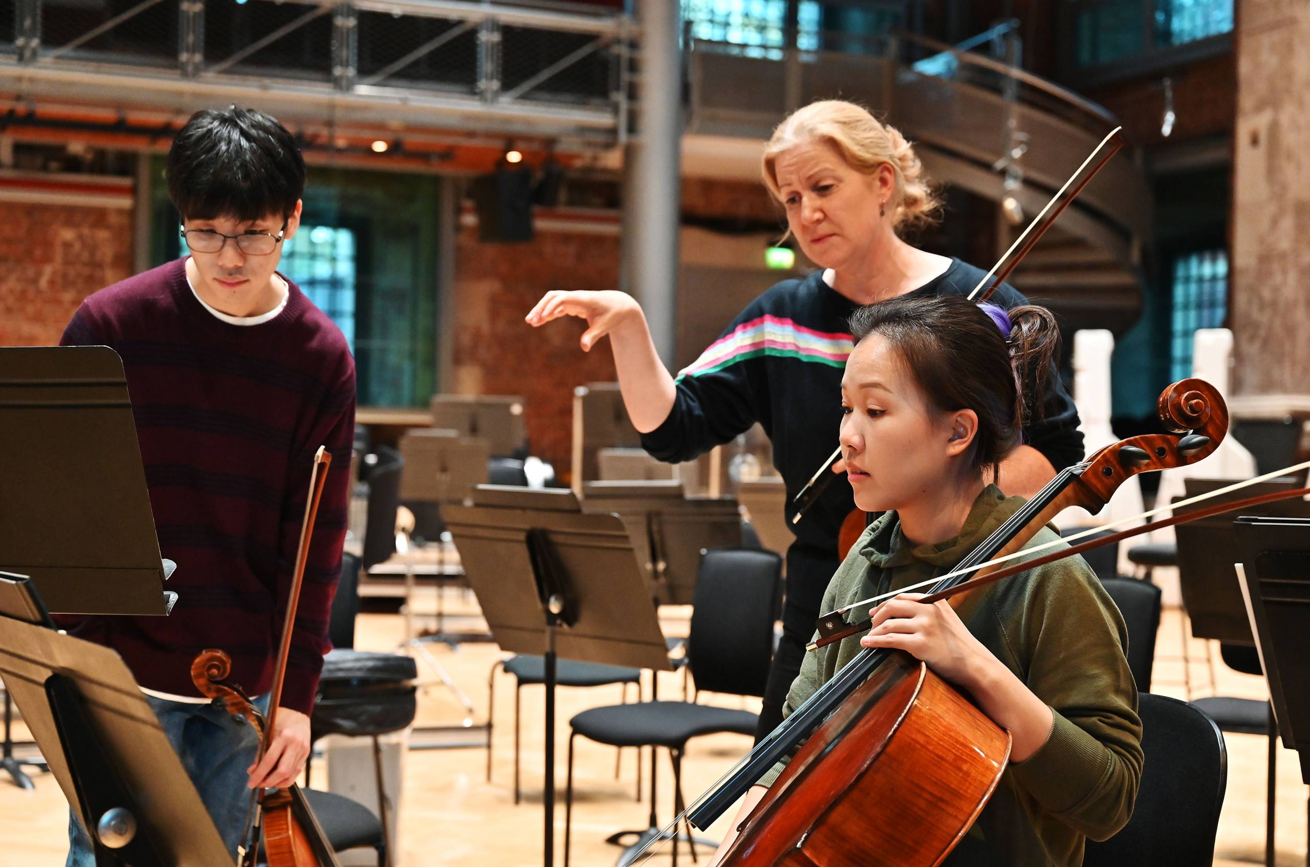 Stood behind a person with a cello, an LSO musician points towards something in the sheet music in front of them.