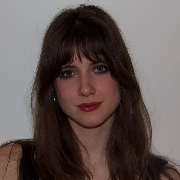 A close-up portrait of Connie Harris with long brunette hair and bangs, featuring bold red lipstick and dark eyeliner against a neutral background.